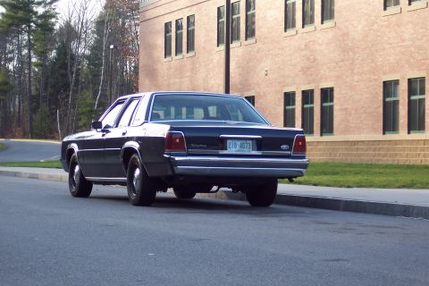2001 Ford Crown Victoria - A dark sedan is parked on the street in front of a brick building.