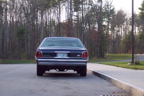 2001 Ford Crown Victoria - Rear view of a dark 2001 Ford Crown Victoria parked on asphalt with a concrete curb and trees in the background.