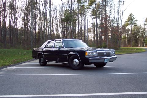 2001 Ford Crown Victoria - Black Ford Crown Victoria parked in a lot with trees in the background.
