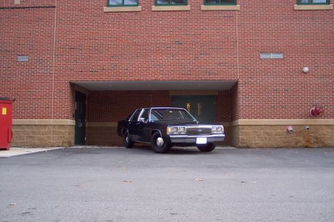 2001 Ford Crown Victoria - A dark-colored sedan is parked in front of a brick building with a covered entryway.