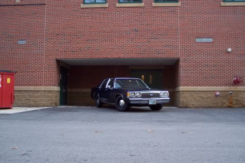 2001 Ford Crown Victoria - A dark blue 2001 Ford Crown Victoria is parked in front of a brick building with a covered entrance.