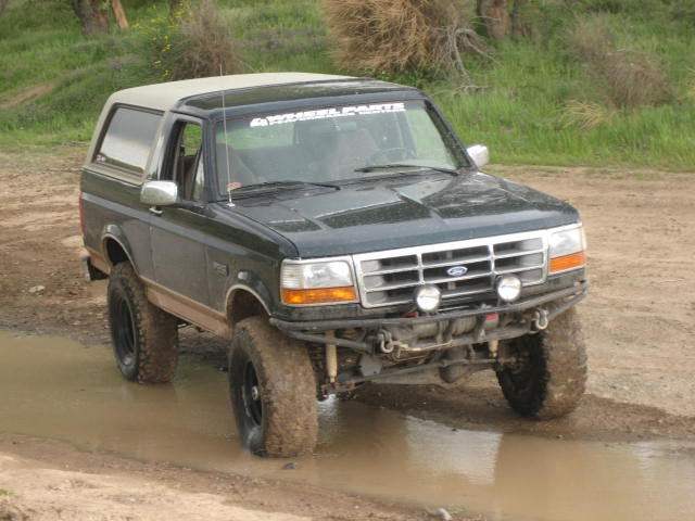1995 Ford Bronco, 3q-front view, dark green with tan top, driving through mud