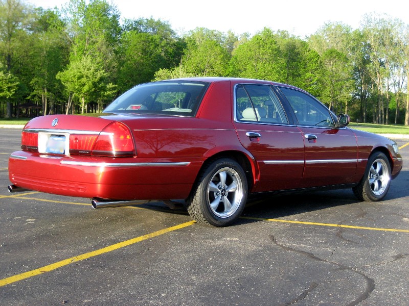 Red sedan parked in a lot, trees in background. It's a 2000 Mercury Grand Marquis