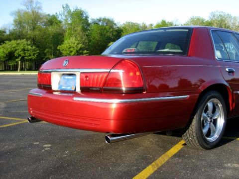 2000 Mercury Grand Marquis - A red 2000 Mercury Grand Marquis sedan is shown from the rear quarter angle, parked on asphalt with yellow lines on asphalt.