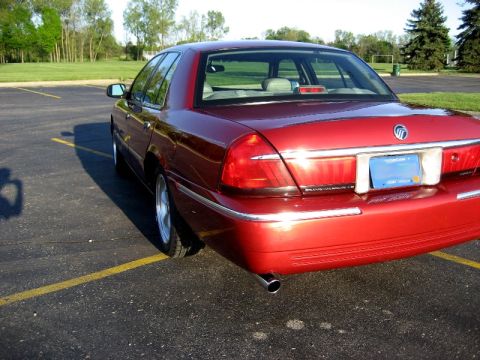 2000 Mercury Grand Marquis - Rear view of a red 2000 Mercury Grand Marquis parked in an asphalt lot with yellow lines.