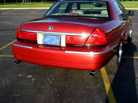 2000 Mercury Grand Marquis - The rear of a red sedan is parked in a lot, showing its taillights and dual exhaust pipes.