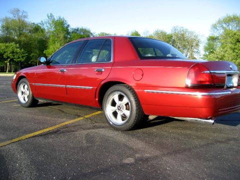 2000 Mercury Grand Marquis - A red sedan is parked in a lot under a clear sky with trees in the background.