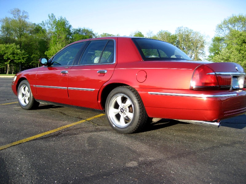Red sedan parked on asphalt, viewed from rear quarter angle. Chrome trim and alloy wheels are visible