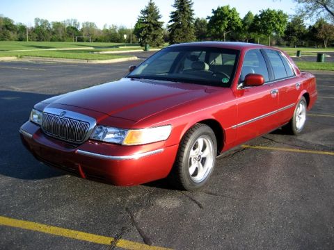 2000 Mercury Grand Marquis - Red 2000 Mercury Grand Marquis sedan parked in a lot with trees and grass in the background.