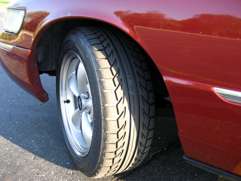 Close-up of a car's front passenger-side wheel and fender. The car is red
