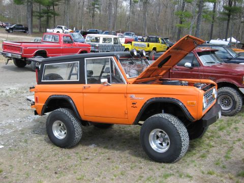 1977 Ford Bronco - An orange Ford Bronco is parked with its hood up, surrounded by other trucks and vehicles.