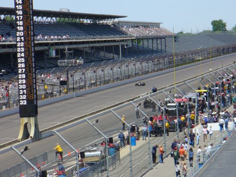 1991 Ford Probe - A race car speeds down the track at an event, with spectators in the grandstands and crew members in the pit area.