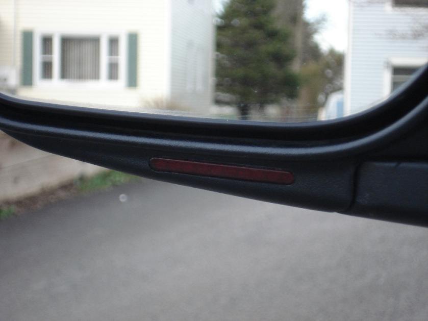 Close-up of red turn-signal repeater lens in a black side mirror housing