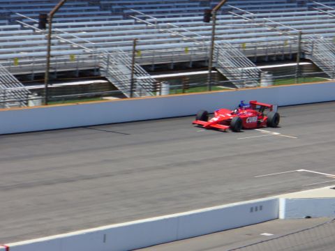 1991 Ford Probe - A red open-wheel race car with 'CURB' visible on its side drives on a race track with grandstands in the background.