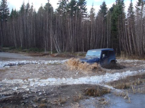 1996 Ford Bronco - A blue Jeep Wrangler navigates a challenging off-road path covered in mud and ice.