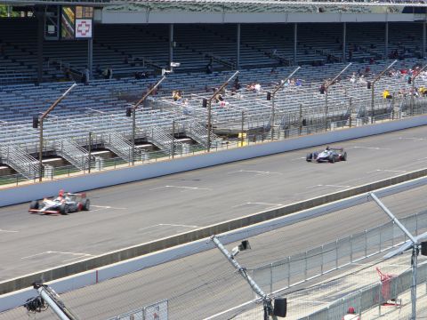 1991 Ford Probe - Two open-wheel race cars speed down a track, with spectator seating visible behind a fence.