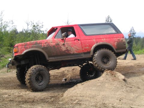 1989 Ford Bronco - A red Ford Bronco navigates an off-road course with a person watching in the background.