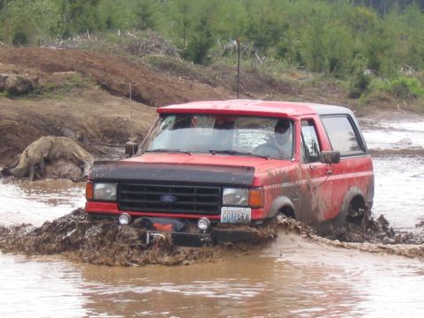 1989 Ford Bronco - A red Ford Bronco navigates a muddy off-road course, its license plate reading GOTPLFX.