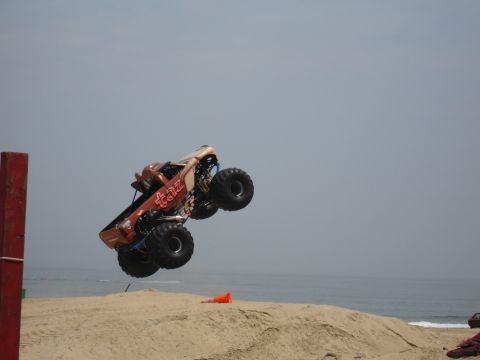 1996 Ford Bronco - A monster truck soars through the air over a beach, with the ocean visible in the distance.