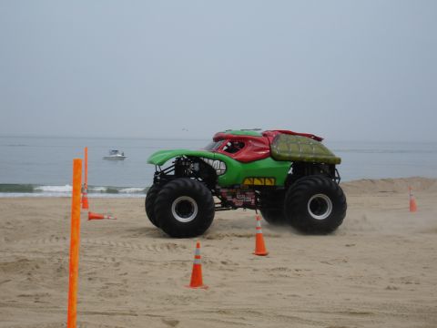 1996 Ford Bronco - A custom monster truck with a turtle-themed body is on a sandy beach with orange cones.