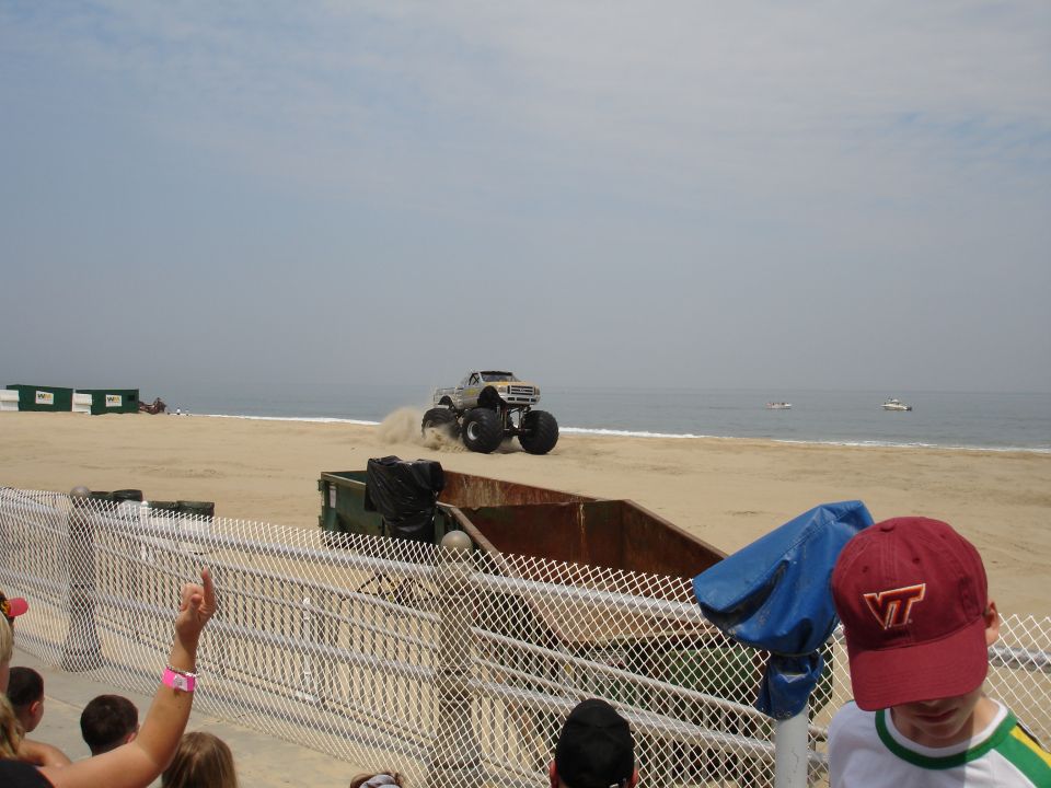 Monster truck kicking up sand on a beach with the ocean in the background
