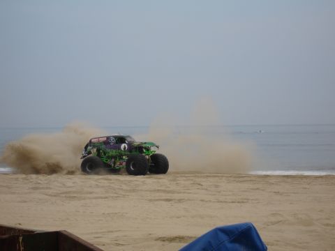 1996 Ford Bronco - A monster truck drives on the sand near the ocean, creating a large dust cloud.