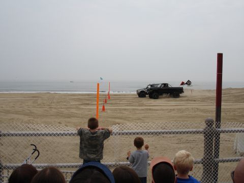 1996 Ford Bronco - A modified truck competes on a beach course with spectators watching.