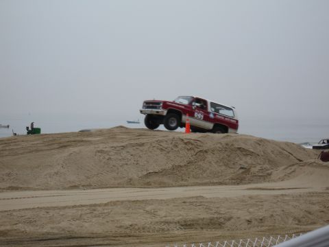 1996 Ford Bronco - SUV with racing decals navigates a sandy terrain by the sea.