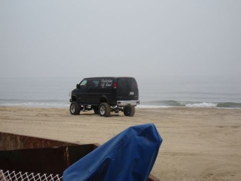 1996 Ford Bronco - A modified black van sits on a sandy beach with the ocean in the background.