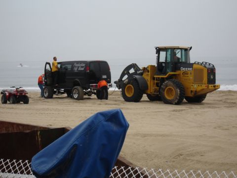 1996 Ford Bronco - A black van and a yellow front loader are on a beach, with people working around the van.