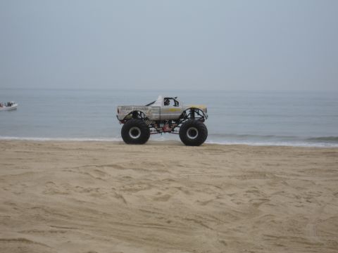1996 Ford Bronco - A monster truck sits on the sand near the water's edge, with a boat visible in the distance.