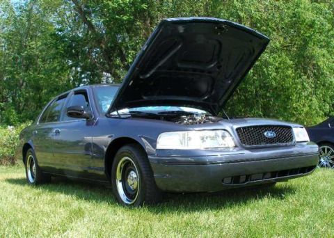 1998 Ford Crown Victoria - A dark blue 1998 Ford Crown Victoria is parked on grass with its hood open, showing the engine bay.