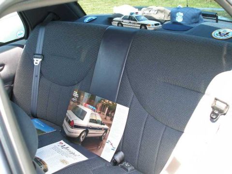 1998 Ford Crown Victoria - A brochure depicting a police car rests on the back seat of a vehicle, next to a police hat.