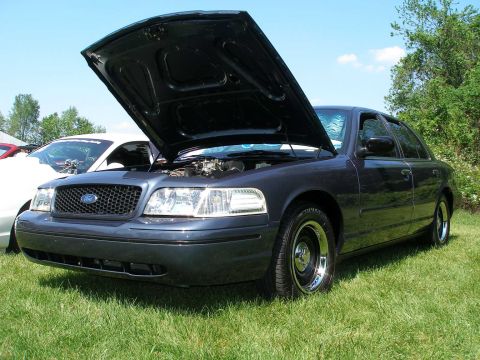 1998 Ford Crown Victoria - A dark blue 1998 Ford Crown Victoria is displayed with its hood open at a car show.