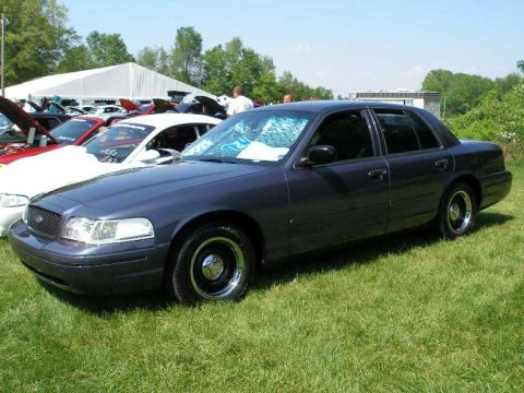 1998 Ford Crown Victoria - Dark blue sedan parked on grass at an outdoor car show event with a tent and other vehicles visible.