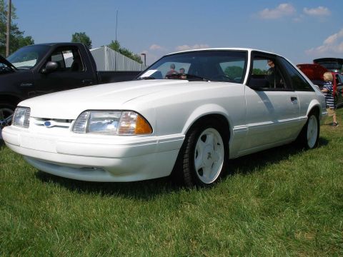 1998 Ford Crown Victoria - White 1993 Ford Mustang hatchback at a car show with a black pickup truck nearby.