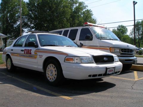 1998 Ford Crown Victoria - A white police car marked "FIRE" and a white van are parked side-by-side in a lot.