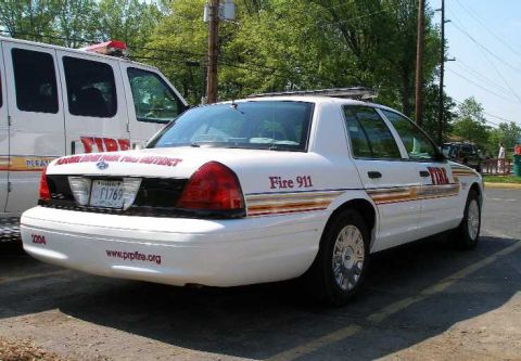 1998 Ford Crown Victoria - White Ford Crown Victoria police car marked for fire department services, parked next to a van.