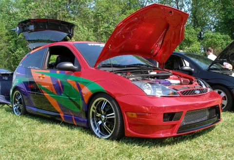1998 Ford Crown Victoria - A red hatchback with custom graphics is displayed with its hood and trunk open at an outdoor car show.
