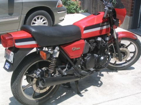 1981 Kawasaki Bayou - A red motorcycle with black seat and distinctive silver and black stripes on the tank and tail section is parked outdoors.