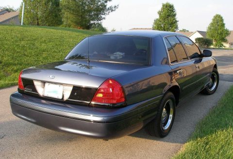 1998 Ford Crown Victoria - Rear view of a 1998 Ford Crown Victoria parked on a paved surface with grass and houses in the background.