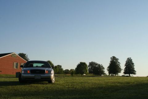 2004 Ford Crown Victoria - A silver 2004 Ford Crown Victoria is parked in a grassy field with a house and trees in the background.