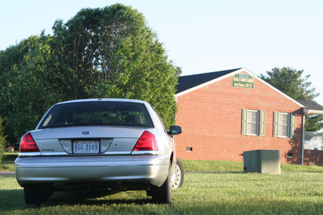 Silver Ford Crown Victoria parked on grass in front of a brick building