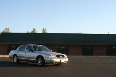 2004 Ford Crown Victoria - A silver 2004 Ford Crown Victoria is parked outside a commercial building under a clear blue sky.