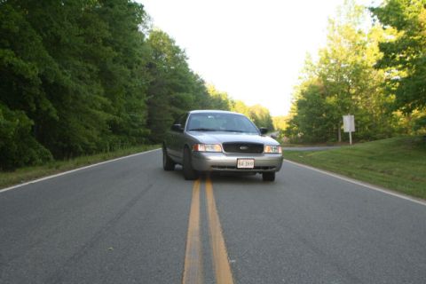 2004 Ford Crown Victoria - Silver 2004 Ford Crown Victoria on a paved road with trees lining the sides.