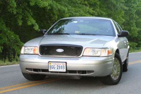 2004 Ford Crown Victoria - A silver 2004 Ford Crown Victoria is shown from the front on a paved road with trees lining the background.