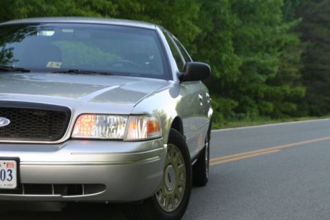 2004 Ford Crown Victoria - A silver 2004 Ford Crown Victoria is seen from a 3/4 front angle on a road with trees in the background.
