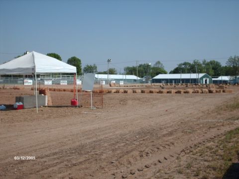 1995 Ford Probe - Outdoor scene with a dirt track, tents, and buildings under a clear blue sky.