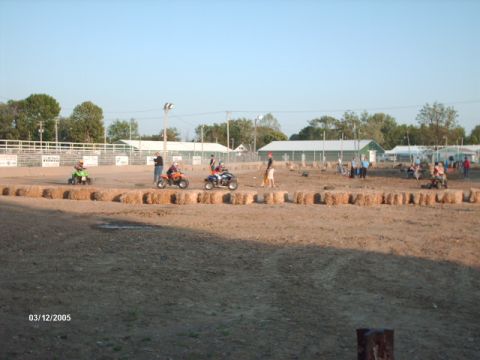 1995 Ford Probe - ATVs race on a dirt track with hay bale barriers and spectators watching.