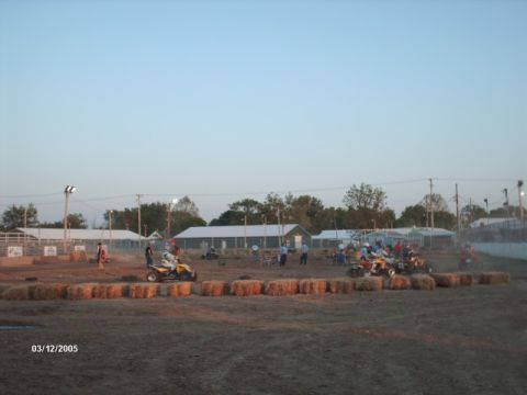 1995 Ford Probe - ATVs compete on a dirt track surrounded by hay bales, with buildings and spectators visible.